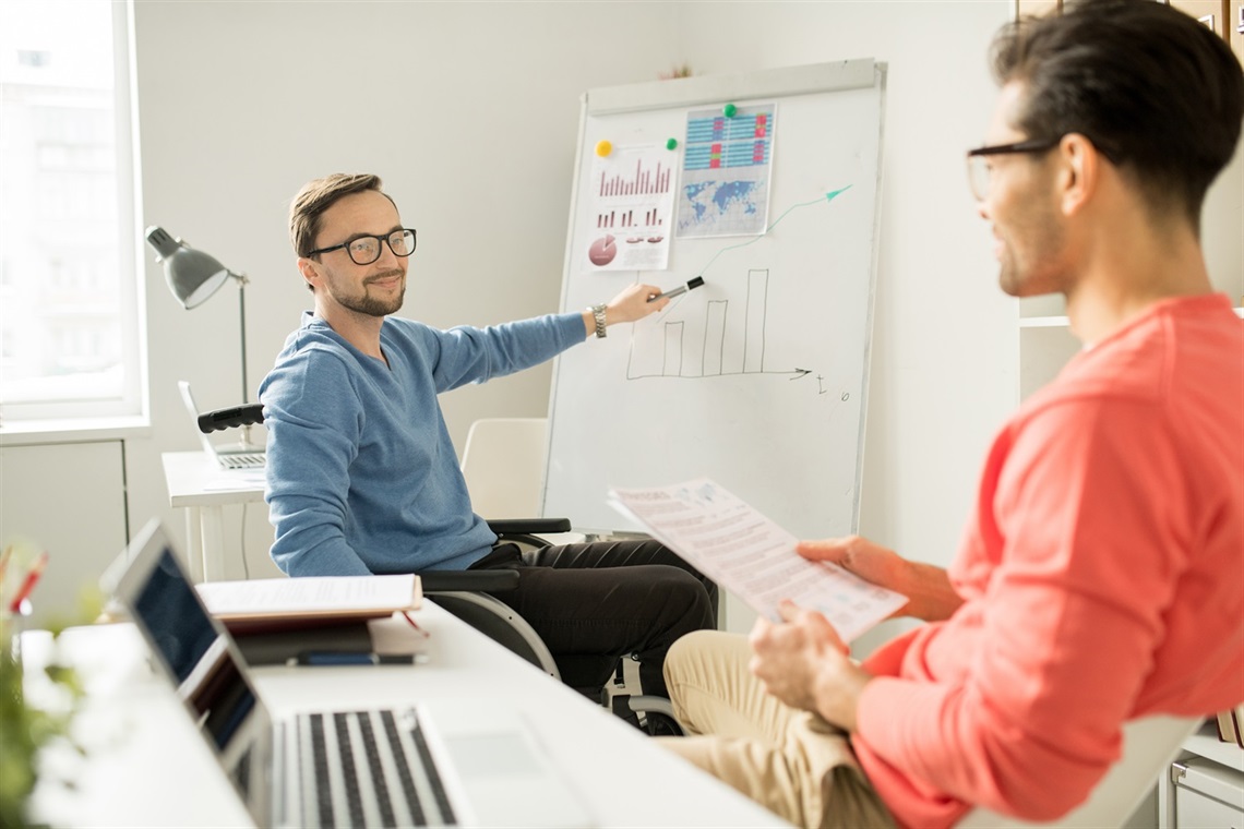 Young man in wheelchair talking with another man in an office.