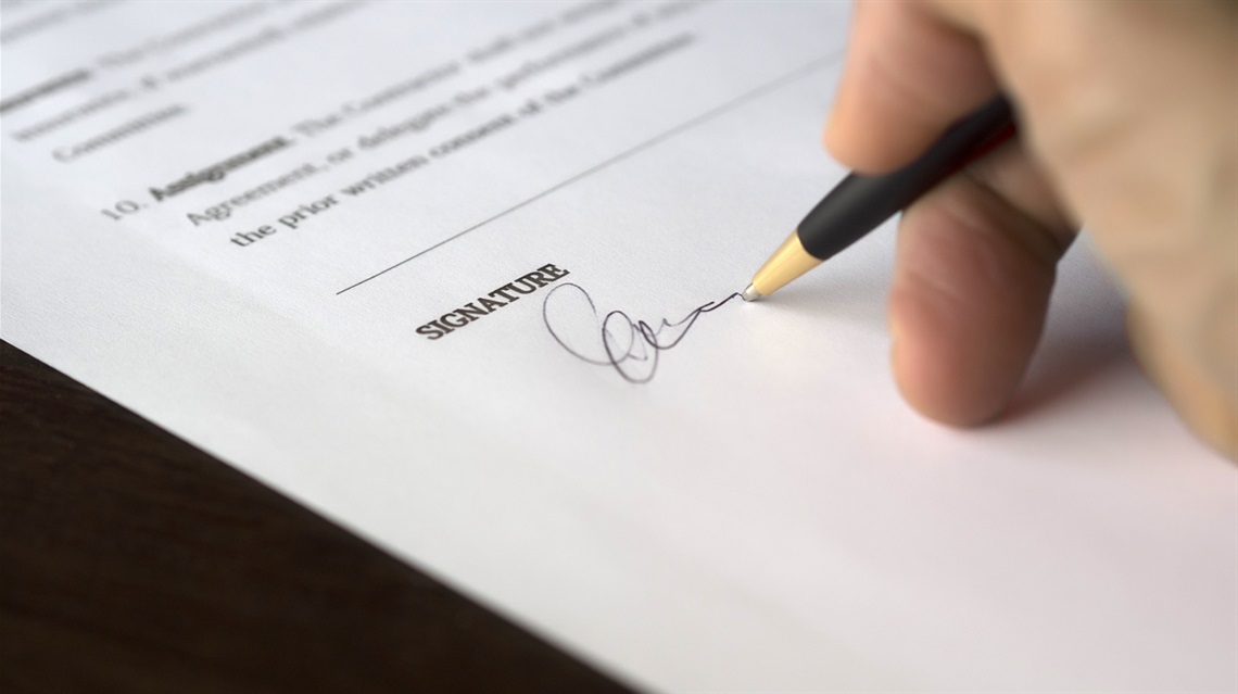 A person writing their signature on a piece of papers