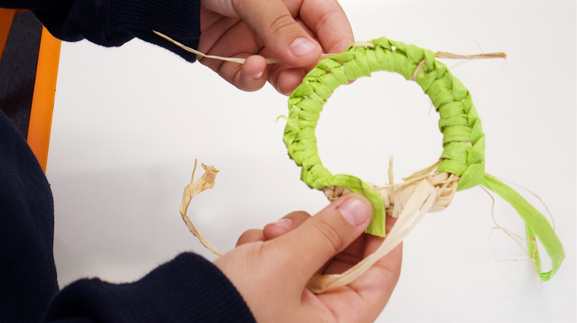 Close up photo of child weaving a circle with green material