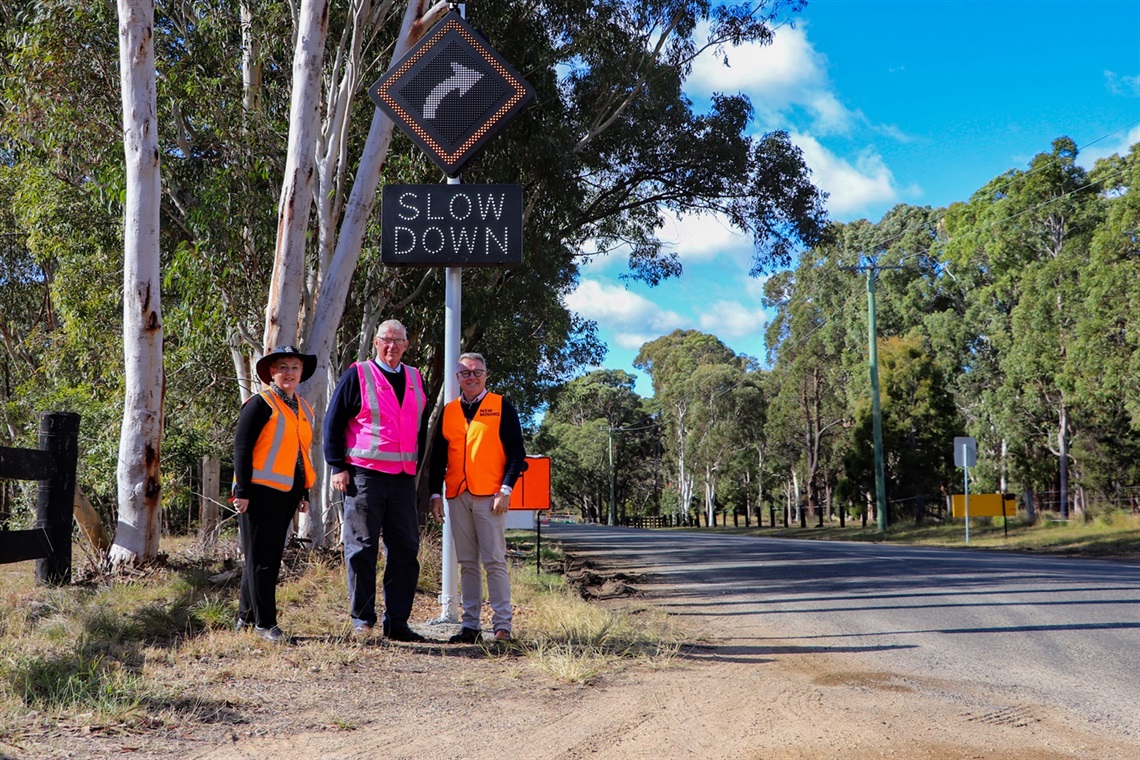 A photo of Council's Road Safety Officer Alison Shelton, Cessnock City Mayor, Councillor Bob Pynsent and Member for the Hunter, the Hon. Joel Fitzgibbon MP pictured in front of the newly installed vehicle activated warning sign on Sandy Creek Road. 