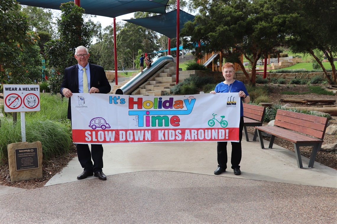 Photo of Cessnock City Mayor, Councillor Bob Pynsent and Council’s Road Safety Officer Alison Shelton at Bridges Hill Park Playground holding up a campaign sign.