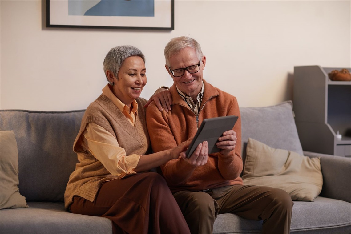 Image of seniors seated on a couch viewing a surface.